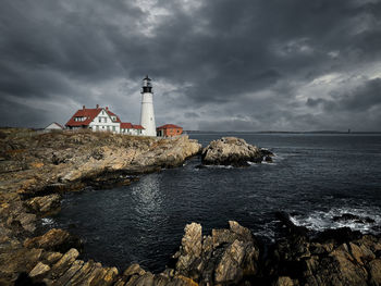 Lighthouse by sea and buildings against sky