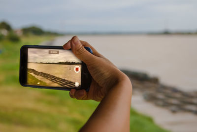 Cropped hand of person photographing lake with smart phone