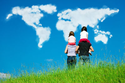 Rear view of father and daughter walking on field against sky