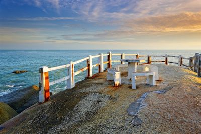 Deck chairs on beach against sky during sunset