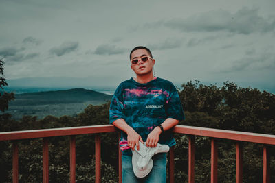 Full length of smiling man standing on railing against sky