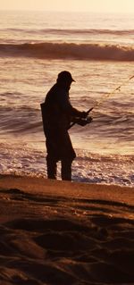 Silhouette man standing on beach against sky during sunset