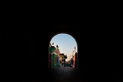 People walking in corridor of arched structure against clear sky