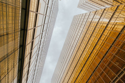 From below facades of similar symmetric skyscrapers with glass mirrored windows under cloudy sky in hong kong