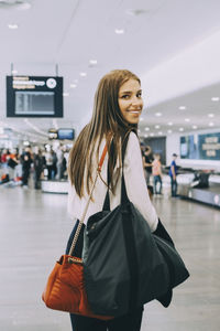 Portrait of smiling young businesswoman walking with colleagues at airport