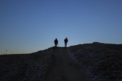 Silhouette people walking on road against clear blue sky