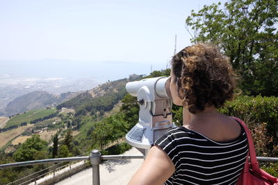 Rear view of woman looking through coin-operated binoculars from observation point at erice