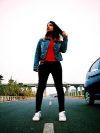 Young woman looking away while standing on car against sky