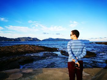 Rear view of woman standing at beach against blue sky