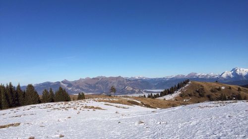 Scenic view of snow covered field and mountains against blue sky