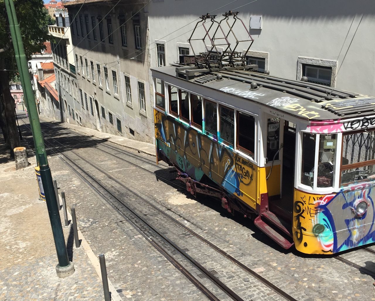 graffiti, building exterior, transportation, built structure, architecture, text, western script, street, railroad track, mode of transport, communication, rail transportation, city, day, outdoors, multi colored, land vehicle, public transportation, no people, sign