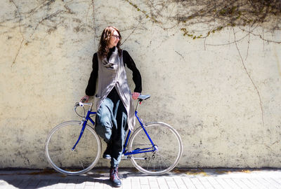 Woman with bicycle standing against wall