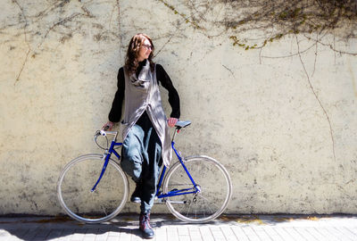 Young woman leaning on a city wall with vintage bike in sunny day