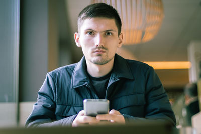 A young man with a phone in his hands is sitting in a diner.