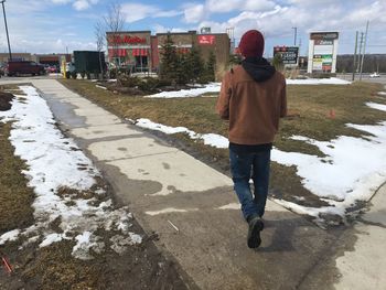 Rear view of man walking on snow in city