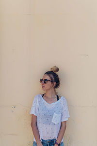 Young woman wearing sunglasses standing against wall