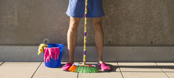 Low section of man with cleaning equipment standing against wall