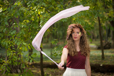 Portrait of woman holding ribbon on stick while standing by trees