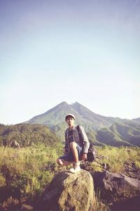 Full length of man sitting on rock against sky