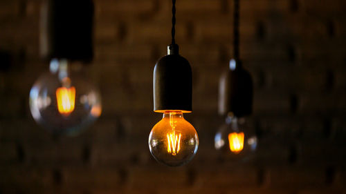 Close-up of illuminated light bulb hanging against wall