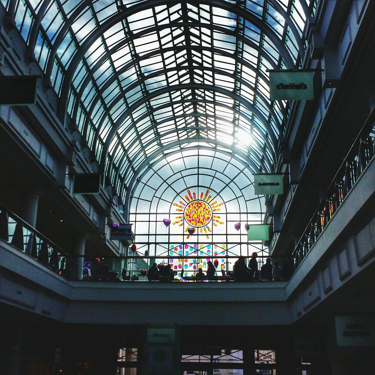 low angle view, ceiling, architecture, indoors, built structure, glass - material, skylight, illuminated, lighting equipment, modern, design, directly below, architectural feature, no people, shopping mall, decoration, window, pattern, day, building