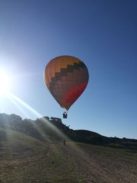 Hot air balloon flying over field against clear sky