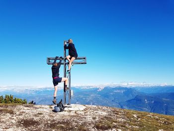 Friends climbing on cross against clear blue sky