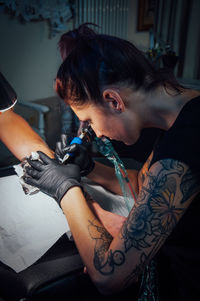 Woman tattooing on customer hand 