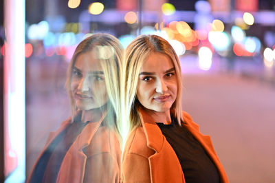 Portrait of smiling young woman in illuminated city at night