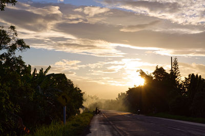 Road amidst trees against sky during sunset