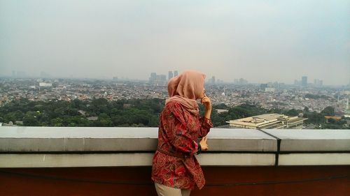 Rear view of woman photographing cityscape against sky