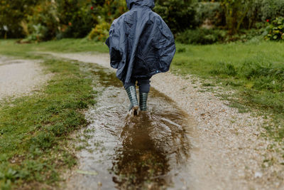Rear view child with rubber boots walking on puddle