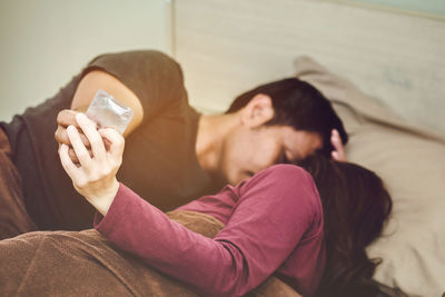 Couple holding condom packet while relaxing on bed at home