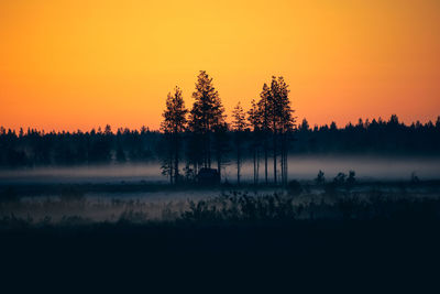 Silhouette trees on landscape against orange sky