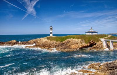 Lighthouse on beach by sea against sky