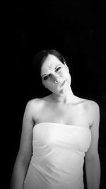 Portrait of young woman standing against black background