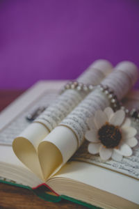 Close-up of koran with prayer beads and flower on table