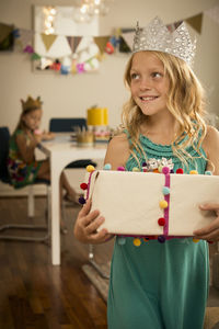 Girl with birthday present looking away while standing at home