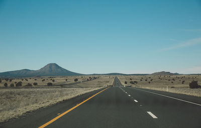 Empty road leading towards mountains against clear sky