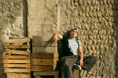 Side view of man sitting near wooden boxes