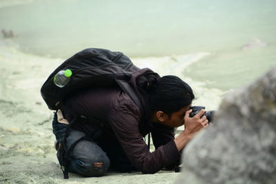 Side view of backpacker photographing with digital camera at beach