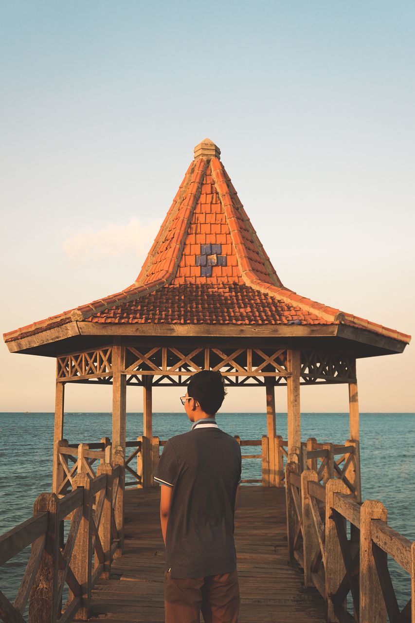 rear view, water, sea, sky, real people, one person, architecture, lifestyles, leisure activity, built structure, nature, scenics - nature, standing, beach, pier, men, horizon over water, beauty in nature, outdoors, looking at view