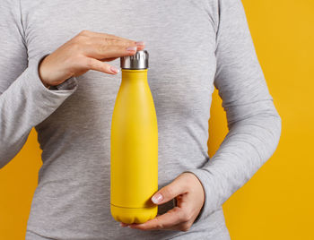 Midsection of person holding yellow bottle against gray background