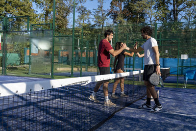 Men and women shaking hands at sports court on sunny day