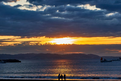 Silhouette people on beach against sky during sunset