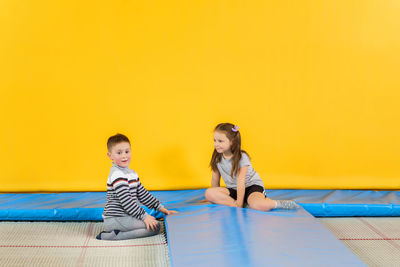 Rear view of boys sitting on yellow wall