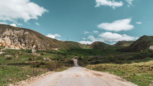 Dirt road leading towards mountains against sky