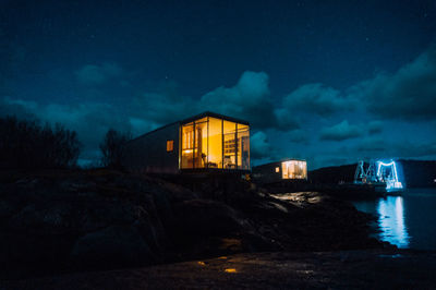 Illuminated house by lake against sky at night