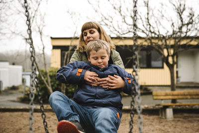 Son with down syndrome taking help of mother while sitting in swing at park