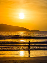 Silhouette man standing on beach against sky during sunset